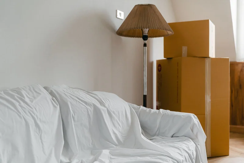 Un canapé bâché et des cartons empilés dans un salon vidé
